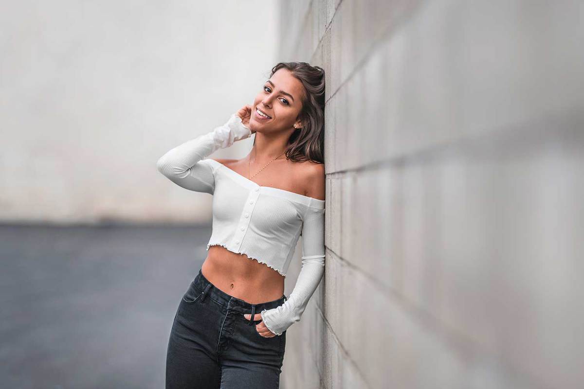 Confident female leaning on a brick wall in the city wearing white crop top and jeans