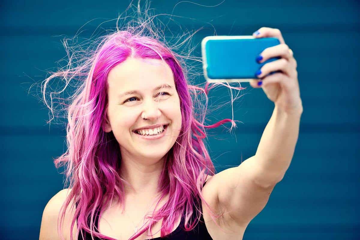 Cute purple-haired young woman smiles mischievously as she takes a selfie