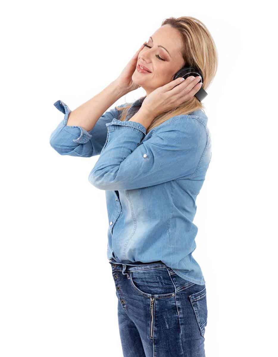 Woman wearing jeans and denim shirt, holding headphone on both ears while enjoying music