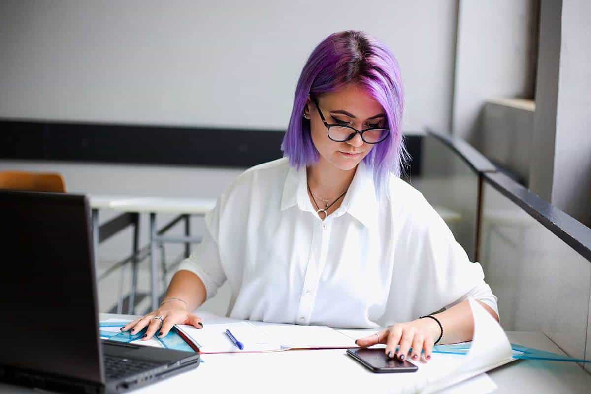 Young women with purple hair looking at her phone while working on some project