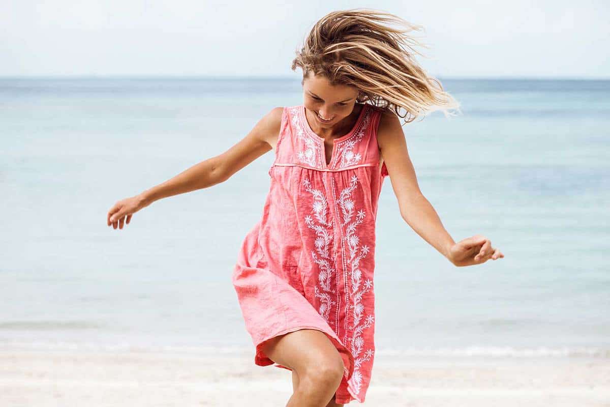 Cheerful woman in dress laughing while walking on the beach