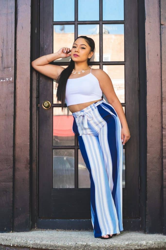 Women in white crop top and blue and white palazzo pants posing in front of wooden door