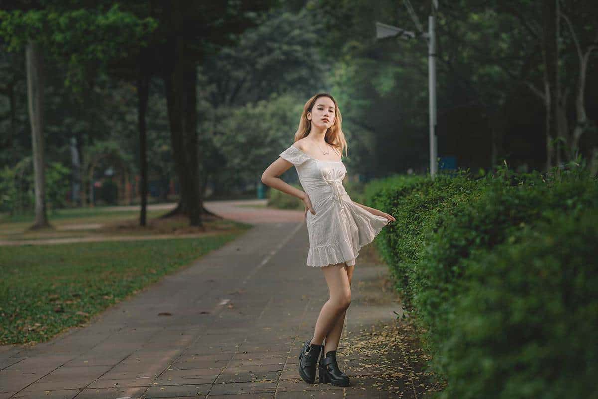 Female teenager wearing white dress and black boots posing at the park