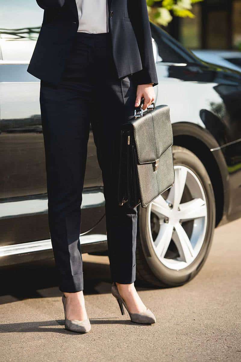 Cropped view of diplomat on grey heels and with briefcase standing near car