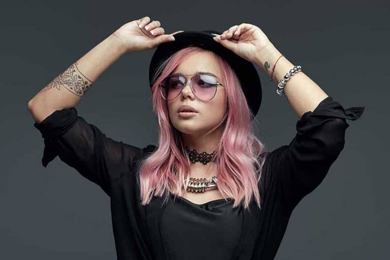 Pink haired woman with tattoos on her body wearing black hat and clothing