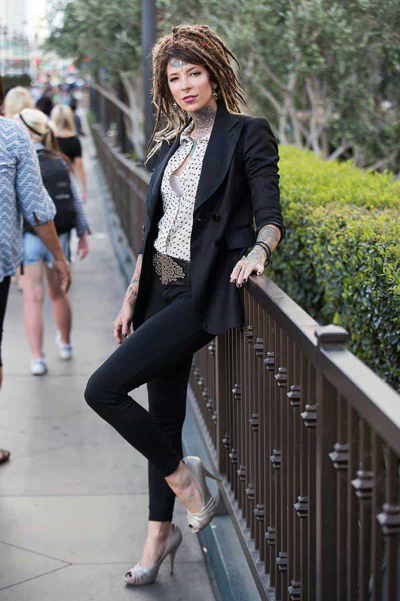 Woman with tattoos and dreadlocks wearing a suit and grey shoes