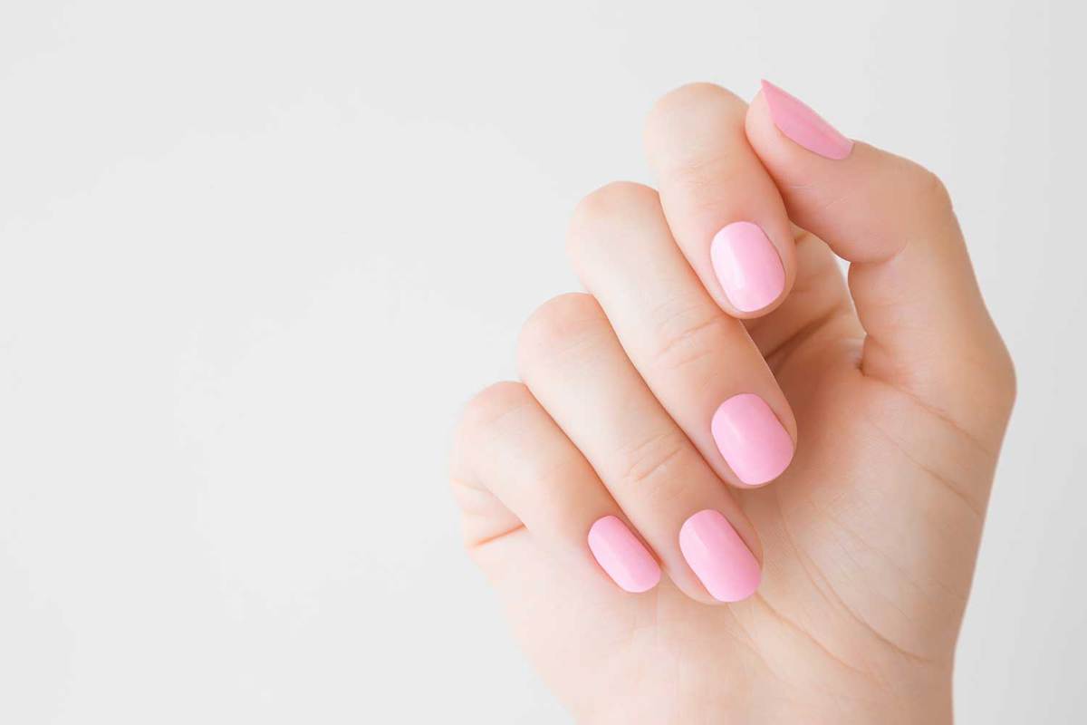 Рука красивой ухоженной женщины с розовыми ногтями на светло-сером фоне
