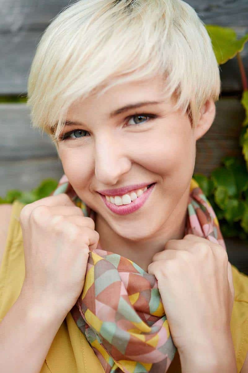 Beautiful short haired platinum blonde woman standing against an ivy fence background