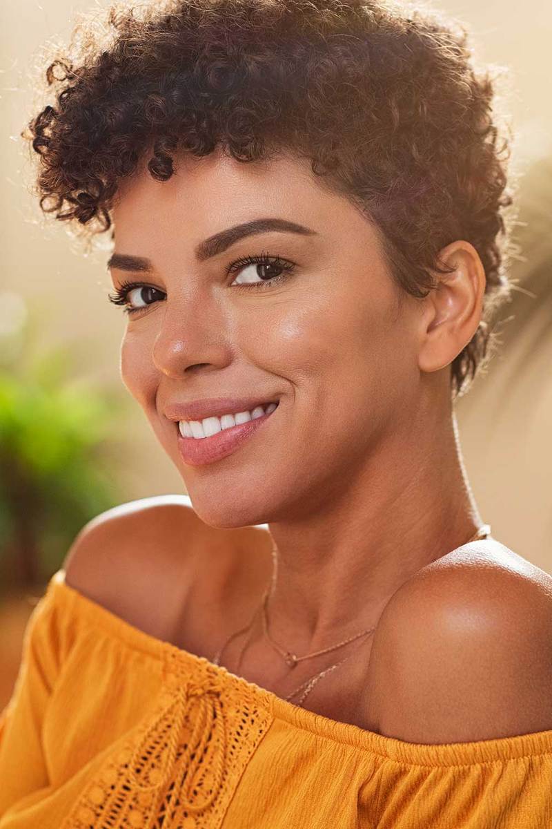Close up face of brazilian young woman with curly short hair smiling and looking at camera
