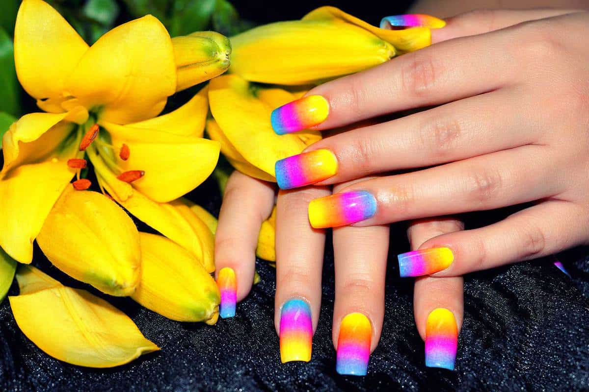 Female hands with colorful nail design holding beautiful yellow flower