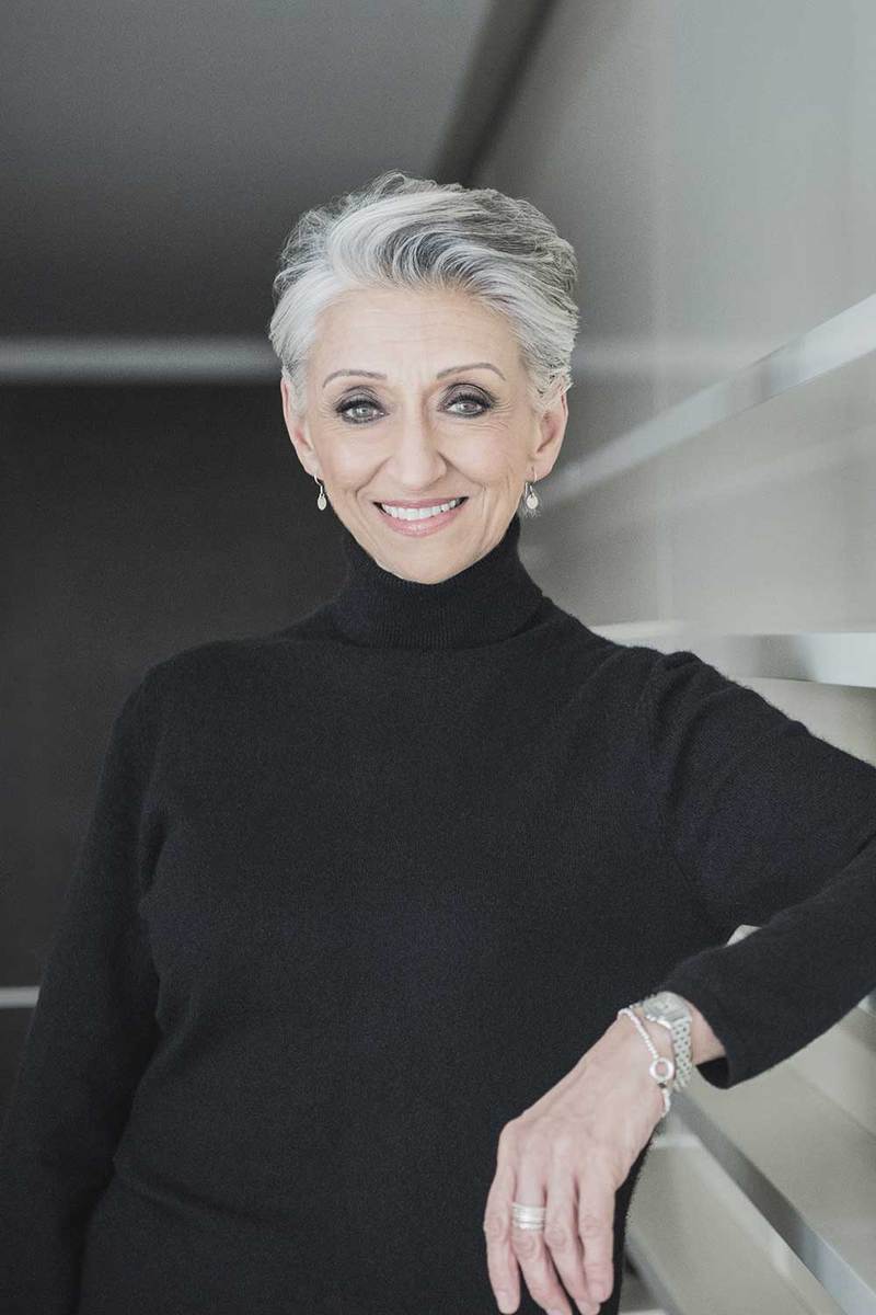 Mature woman with short grey hair wearing black sweater smiling towards the camera