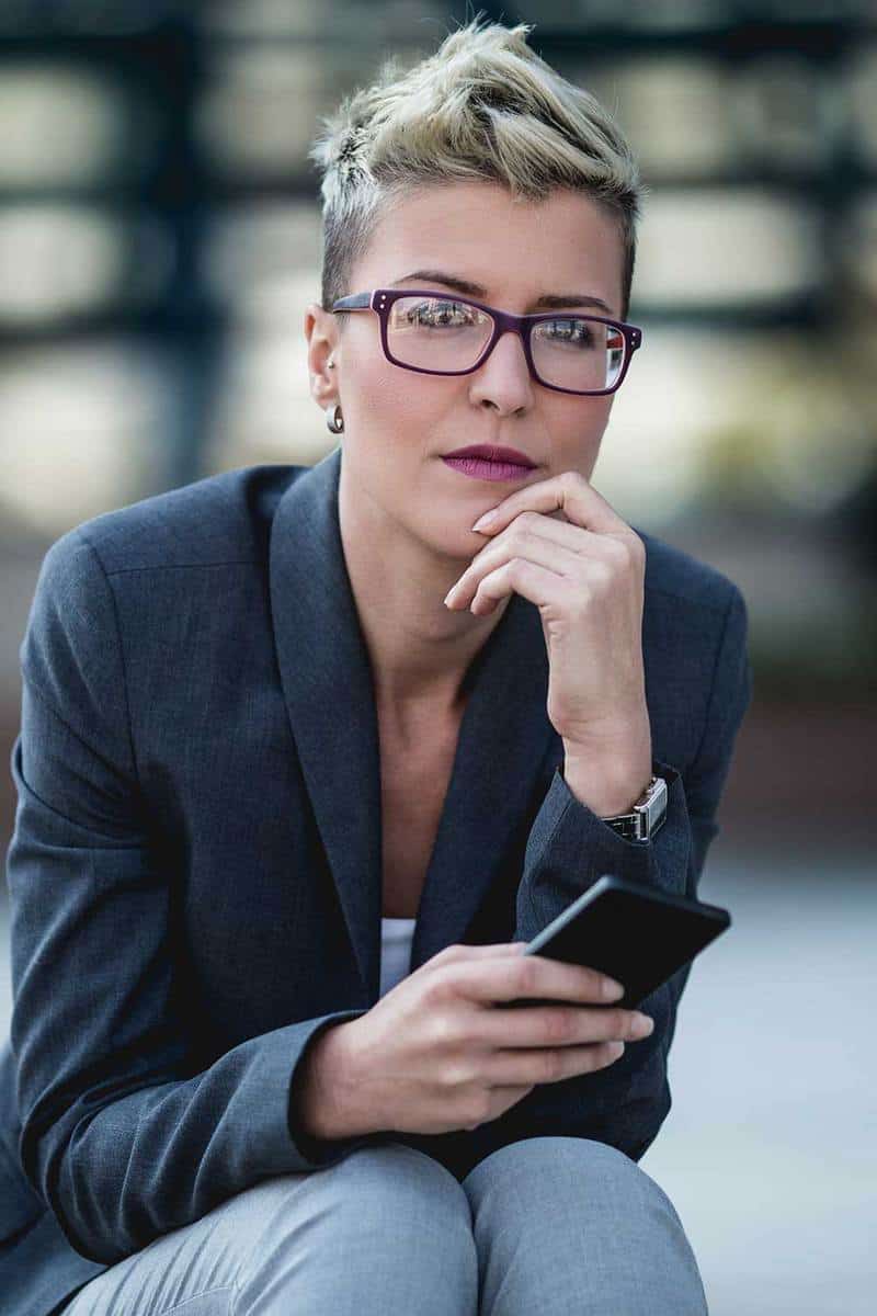 Портрет деловой женщины с короткими волосами, сидящей перед большим современным зданием
