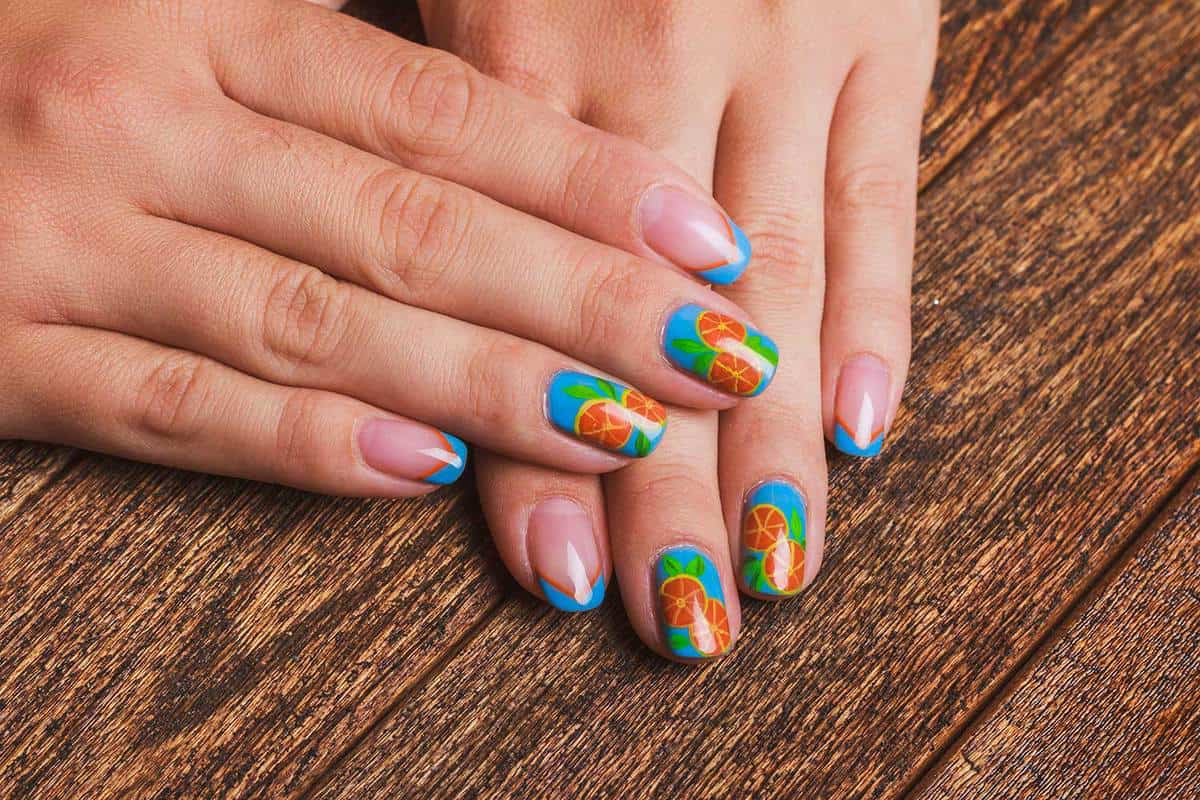 Summer french blue nail art with drawed orange fruit on wooden background