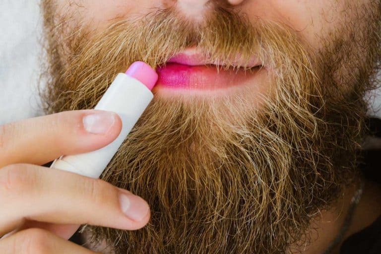 Close up of bearded man applying colorful pink lip balm on his lips, Should Guys Wear Lip Balm?