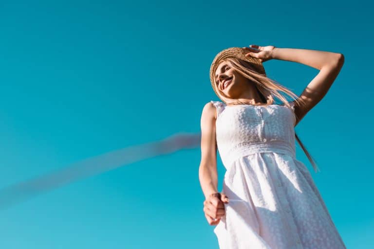 A woman posing happily while wearing a white dress on a blue sky, What Kind Of Dress To Wear As A Guest For A Beach Wedding?