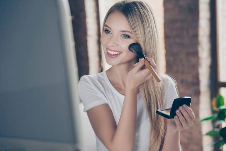 A young woman applying foundation to her face while staring on the mirror, Can You Use Lighter Foundation As Concealer?