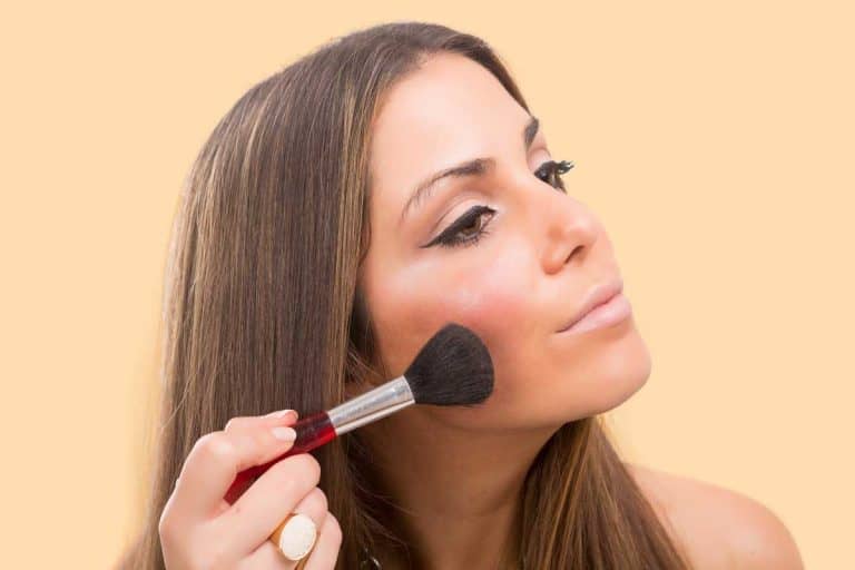 Young beautiful woman applying makeup on her face, Should You Put Bronzer Or Blush On First?