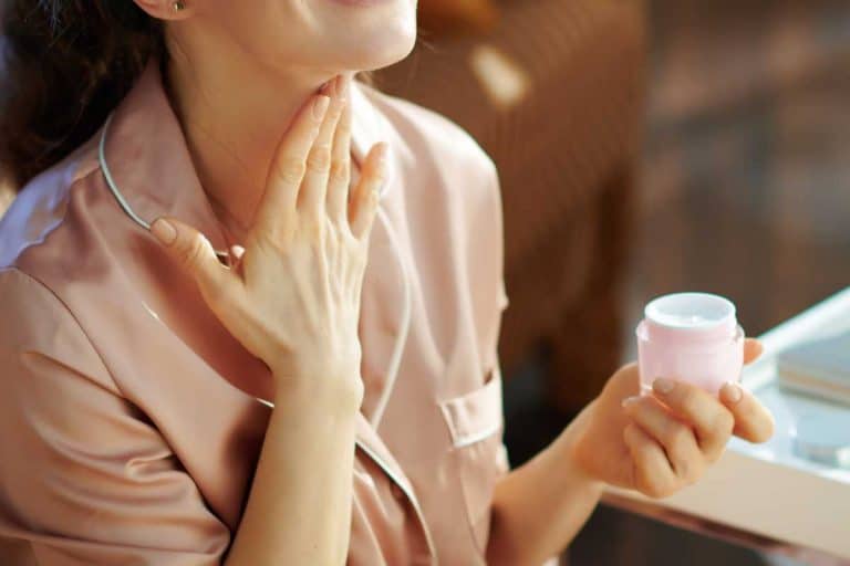 Woman in pajamas with pink cosmetic jar applying neck cream, When Should You Start Using Neck Cream?