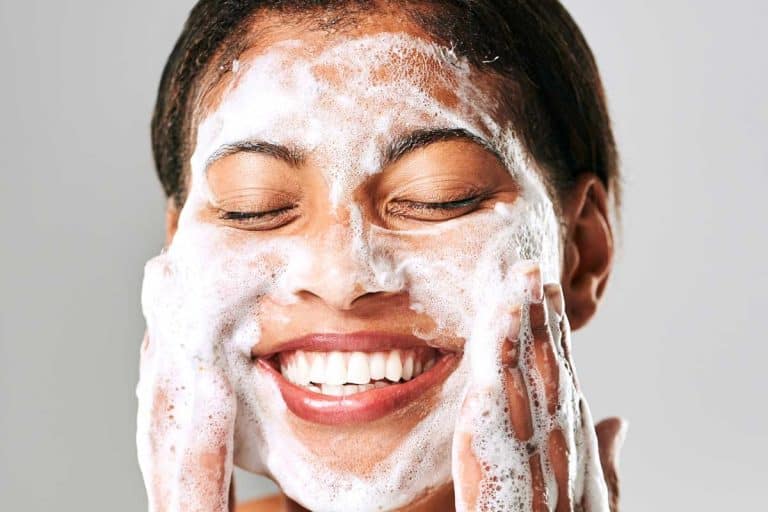 A beautiful young woman washing her face with facial cleanser, How Long Should I Leave Cleanser On My Face?