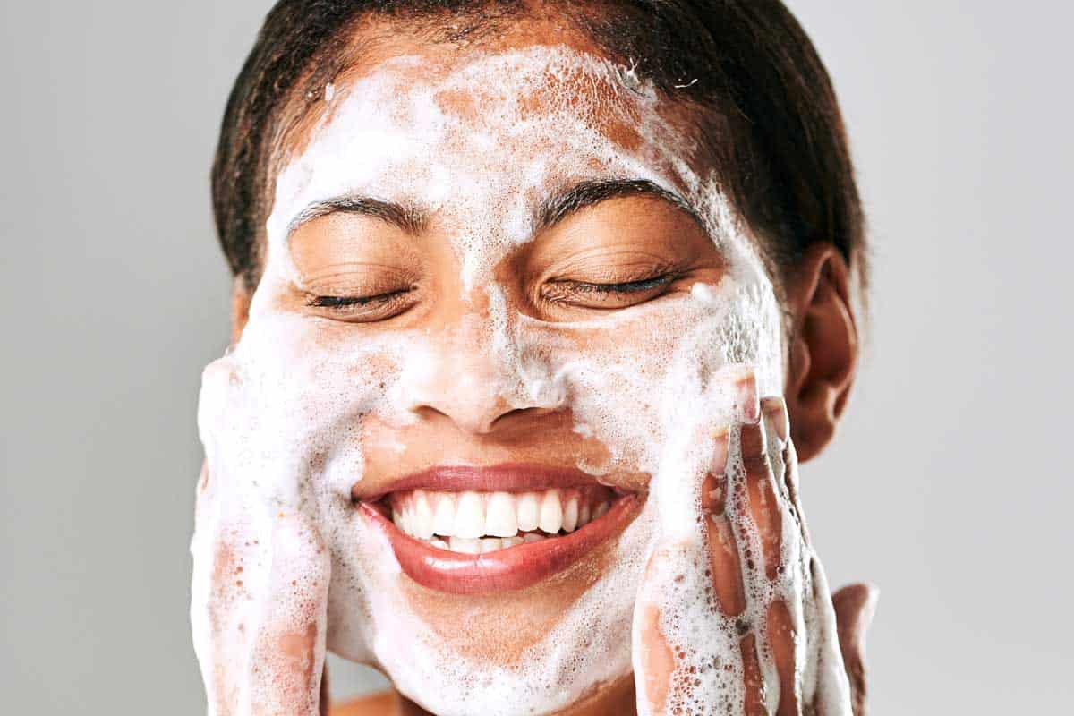 A beautiful young woman washing her face with facial cleanser, How Long Should I Leave Cleanser On My Face?