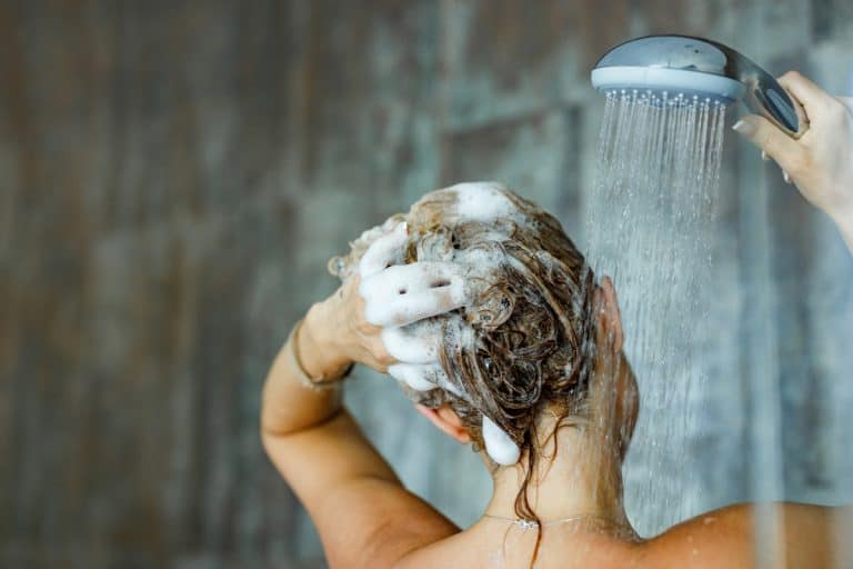 A woman washing off shampoo on her hair with shower spray, Does Wetting Your Hair Everyday Damage It?