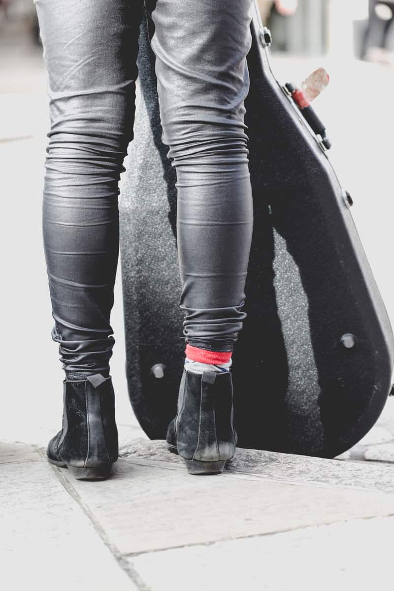 A female street musician wearing gray pants with black Chelsea boots on