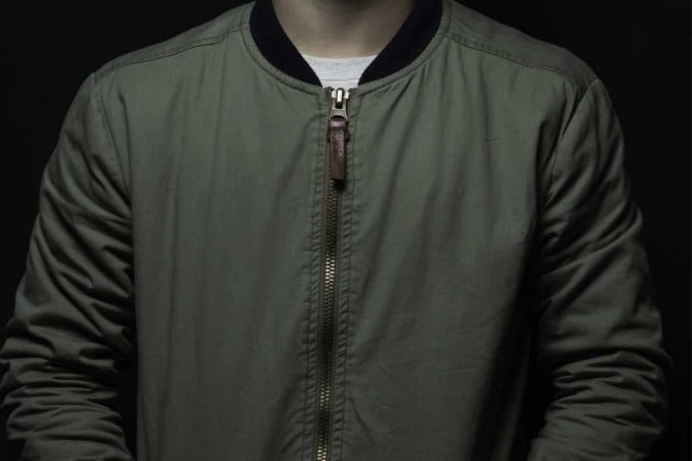 Teen boy posing with bomber jacket in front of black background, Can You Wash A Bomber Jacket? [Here's how to]