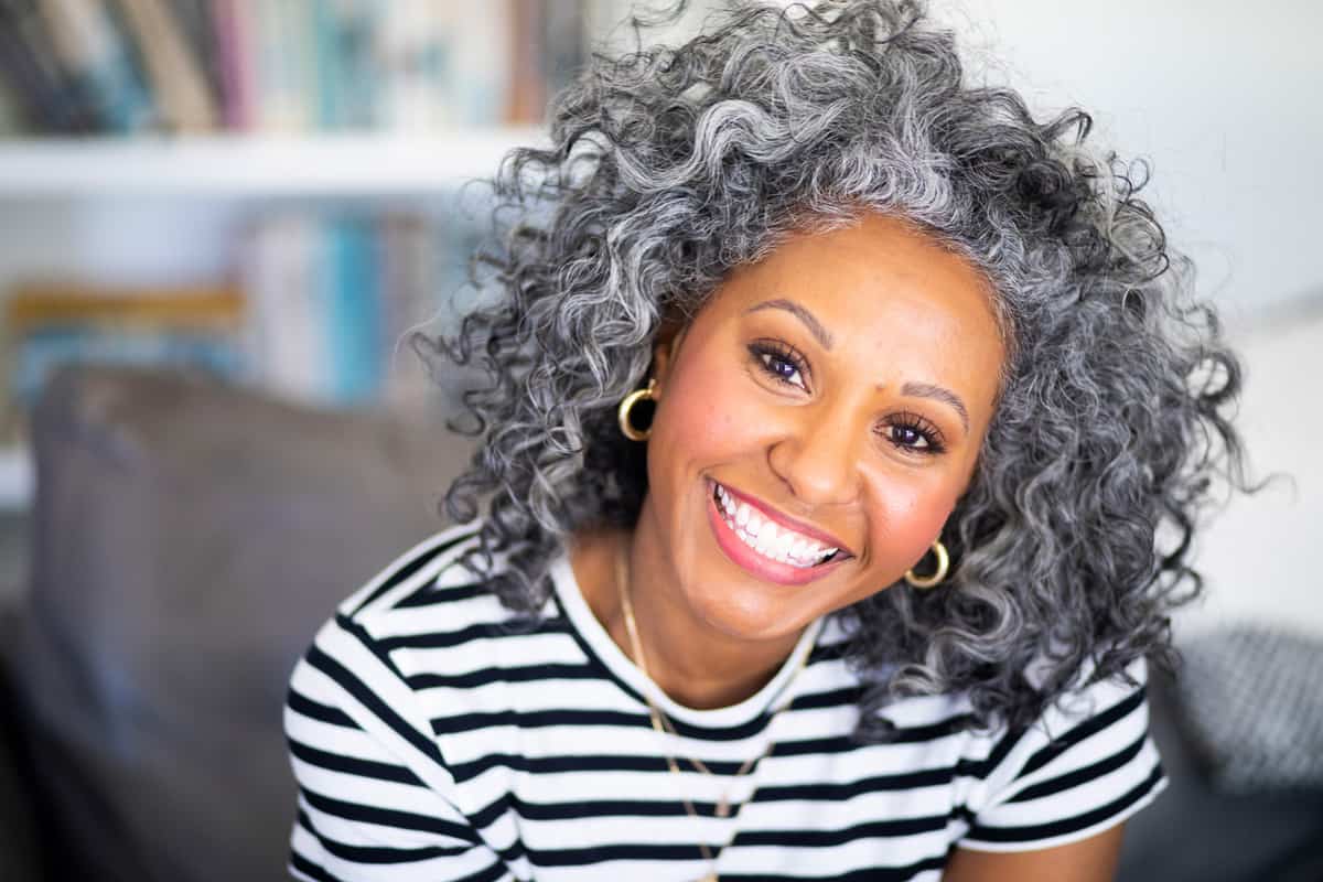 A beautiful black woman with makeup and white curly hair smiles for a headshot
