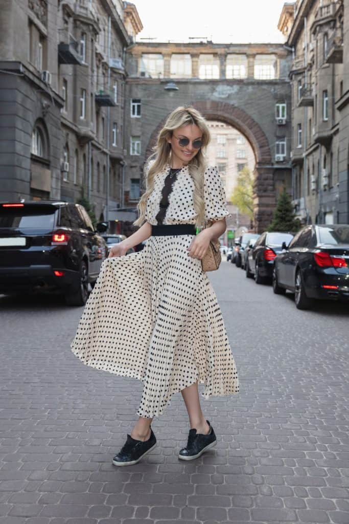 A beautiful blonde woman wearing a maxi dress and black sneakers while posing on the street