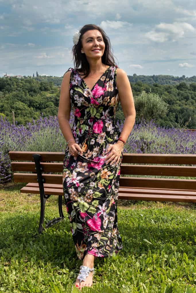 A beautiful Caucasian woman wearing a colorful floral dress lying on a wooden bench with a lavender field on the side