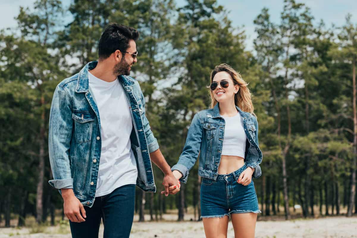A sweet couple holding hands wearing denim jackets on a park