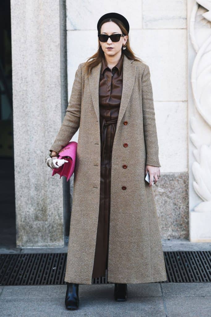 A woman wearing a long coat covering her inner maxi dress and holding her pink purse