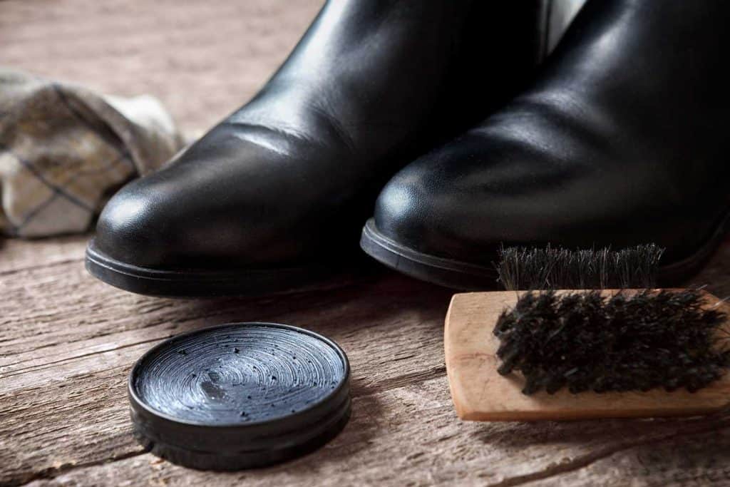 Black boots, polishing cream and brush on wooden table