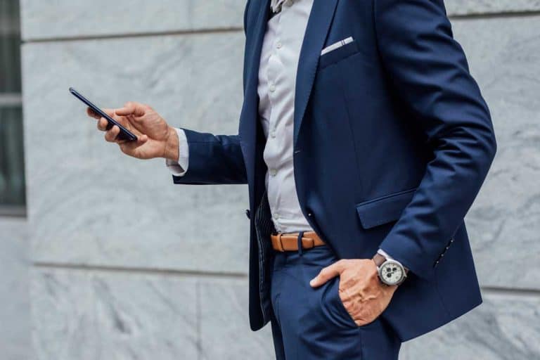 A businessman in a suit using his smartphone outdoors, Should Suit Jacket And Pants Match?