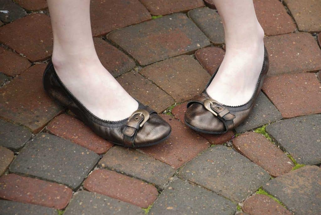 Close up of the feet of a teenaged girl wearing flat shoes with a buckle against brick paving stones