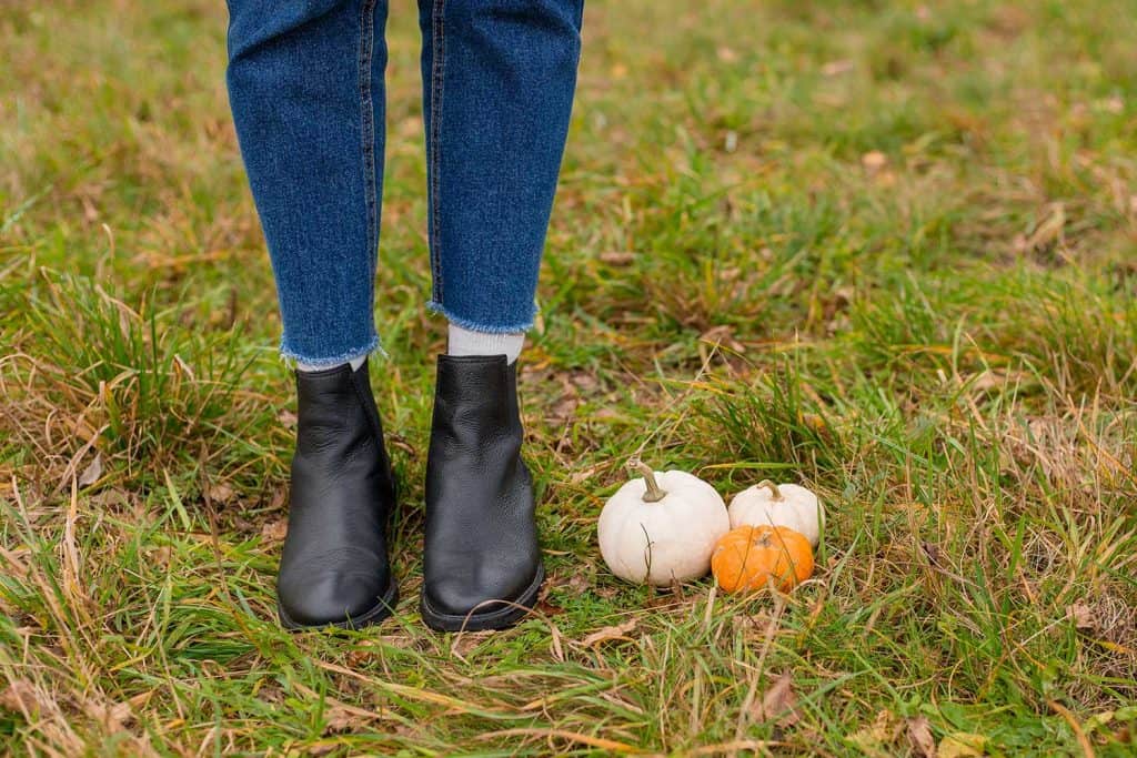Female in Chelsea boots on autumn grass with orange and white pumpkins