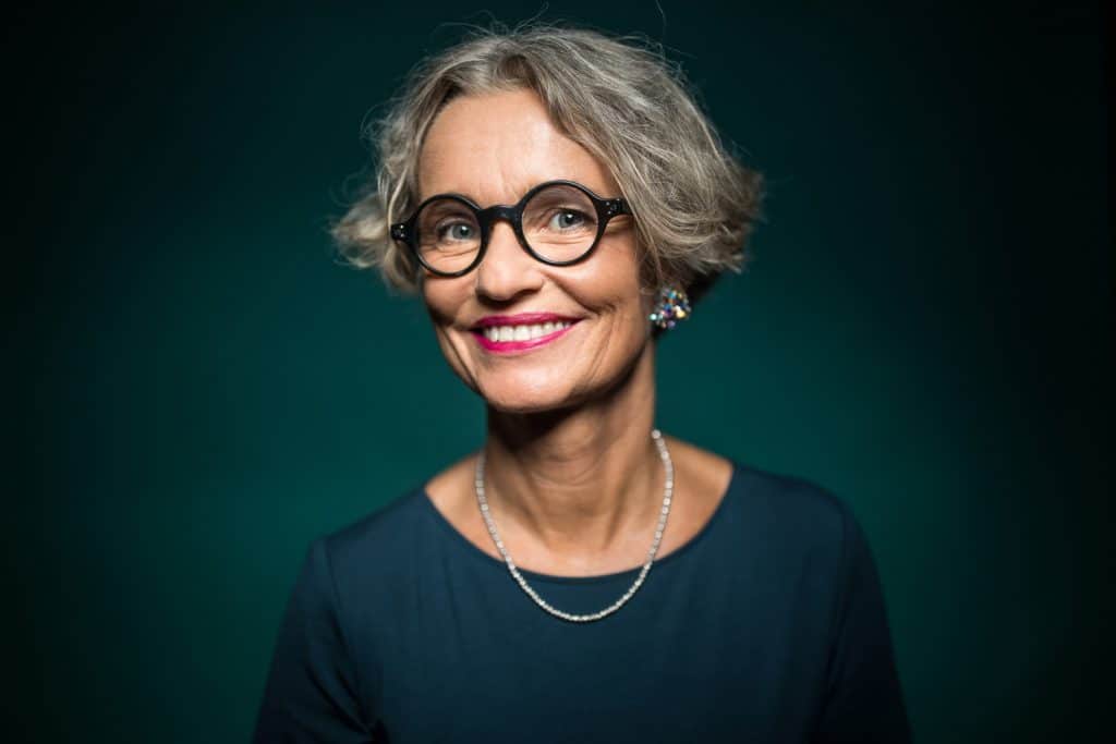 Portrait of cheerful woman with makeup in eyeglasses against green background. Smiling female is wearing jewelry. She is having short gray hair.