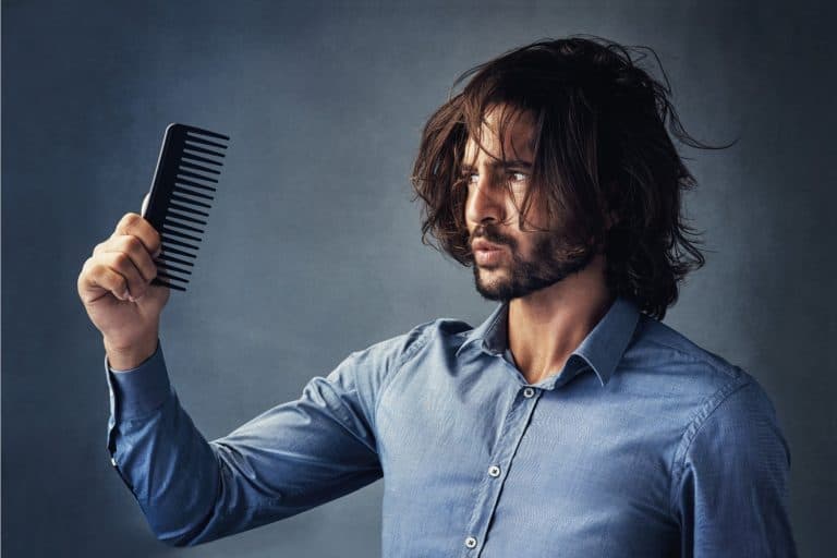 handsome young man looking at his comb while brushing his hair against a grey background