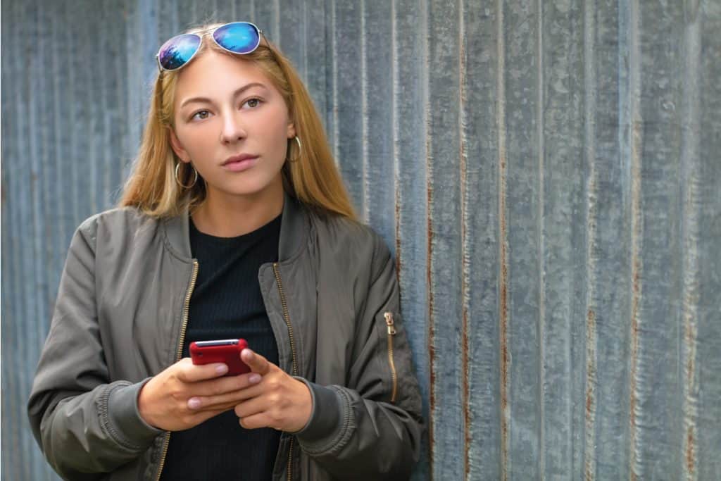 Lady holding a smartphone and wearing a bomber jacket