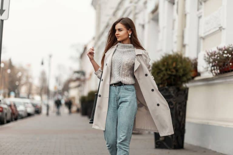 A beautiful woman walking down the street wearing a beige coat and denim pants, What Color Coat Goes With Everything? [5 Great Options With Photos]