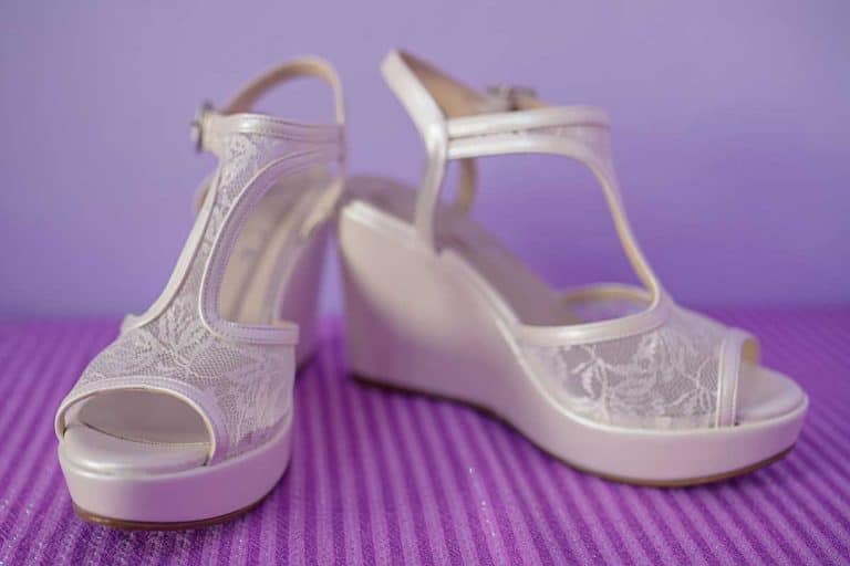 A white platform wedge pumps set against a purple background, Can You Wear Wedge Sandals To A Wedding Or a Black Tie Event?