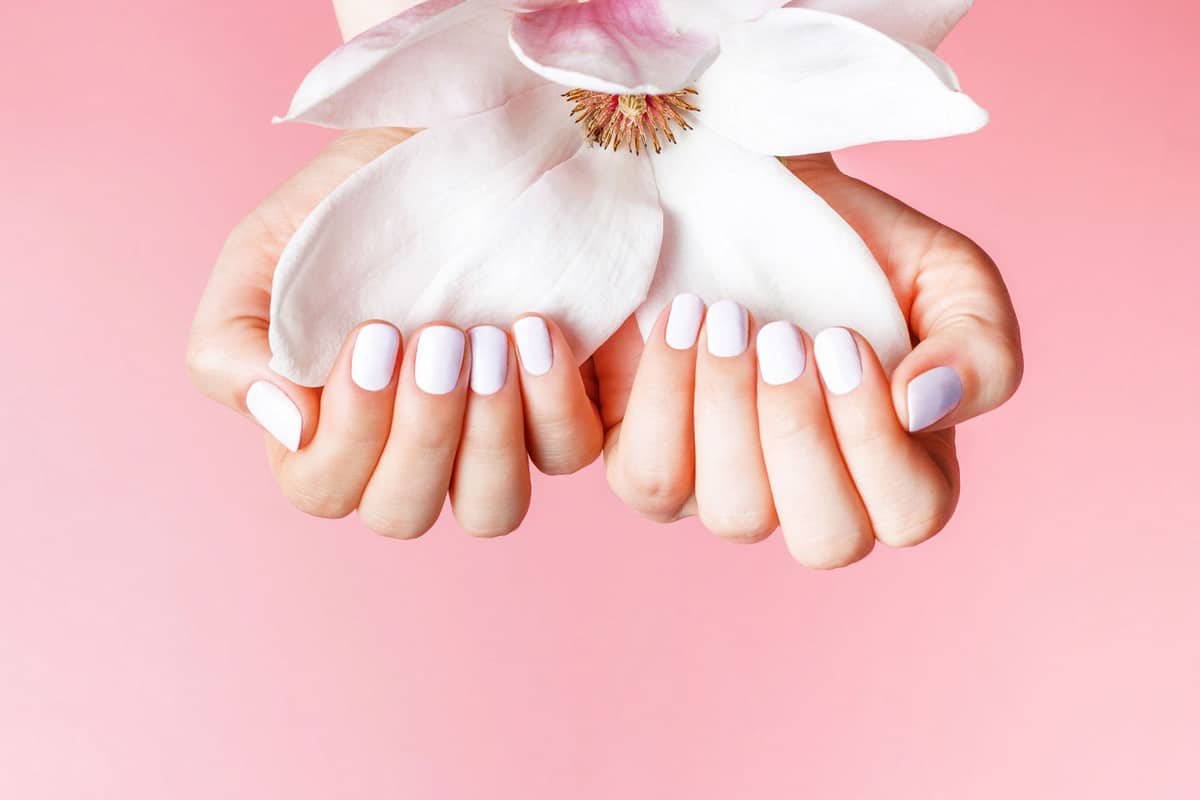 A woman holding a flower while showing her nails polished in white