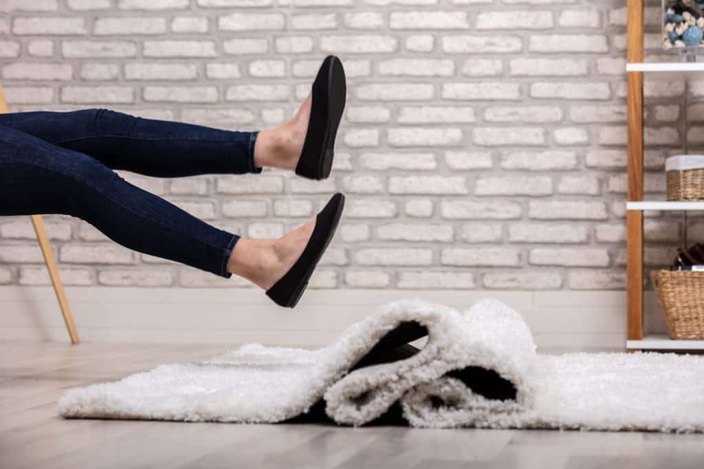 A woman wearing jeans and flats and slipping on the rug