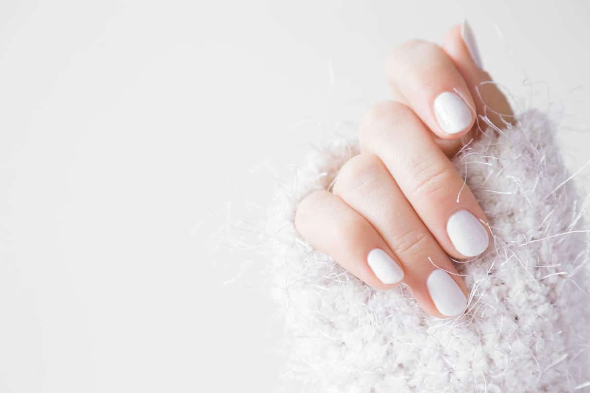 Beautiful groomed woman's hands with white nails on the light gray background, Can You Paint Over Shellac Nails?