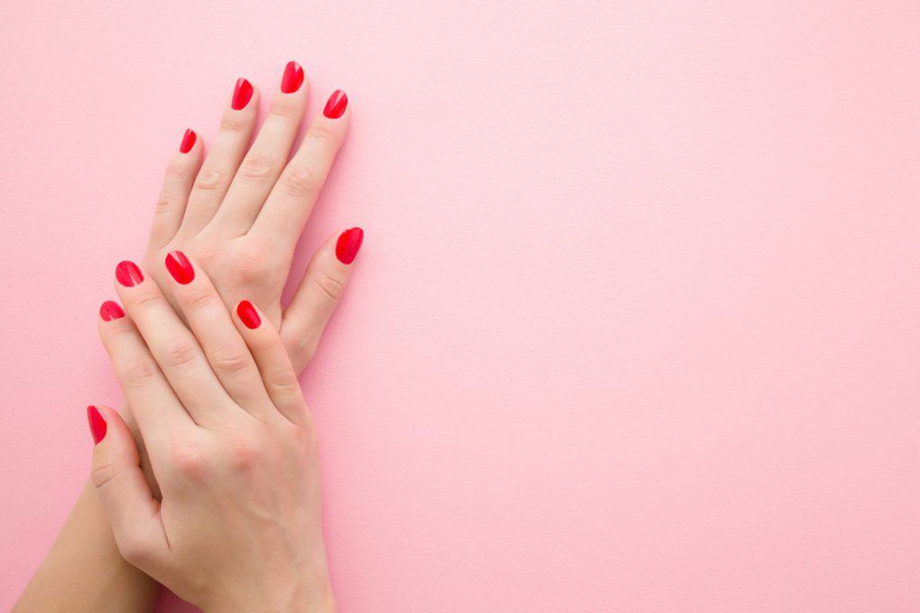 Beautiful woman hands with red nails on light pink table background