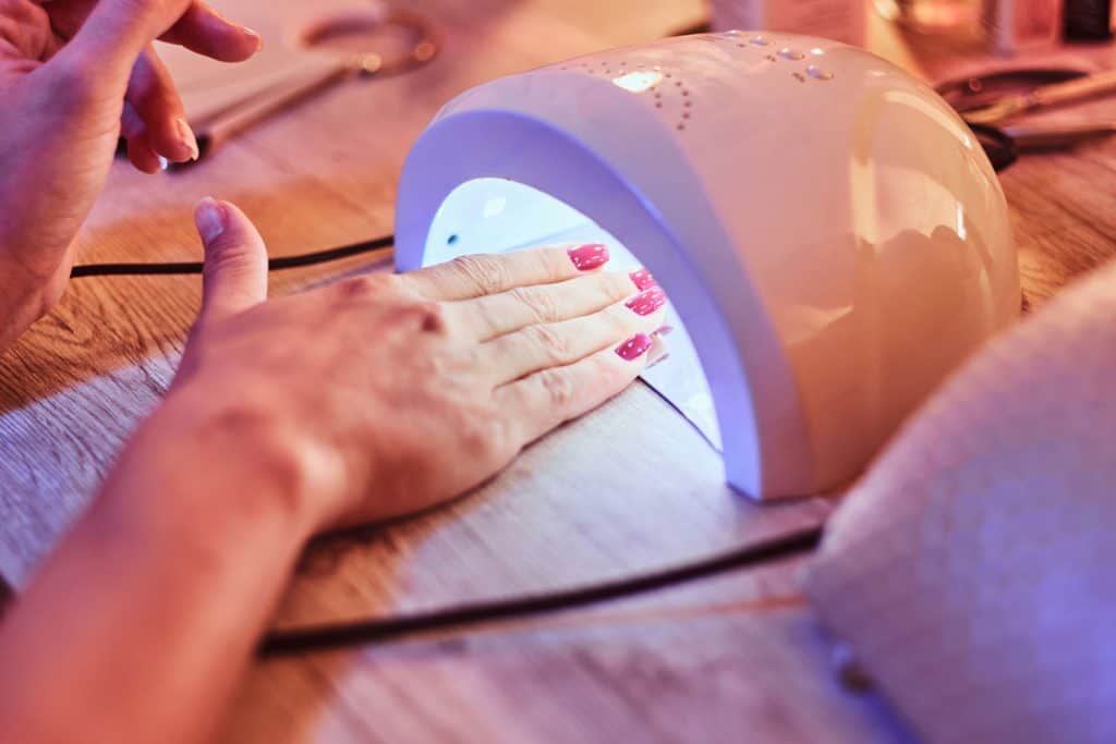 Клиентка с красным лаком в маникюрном салоне сушит полированные ногти ультрафиолетом