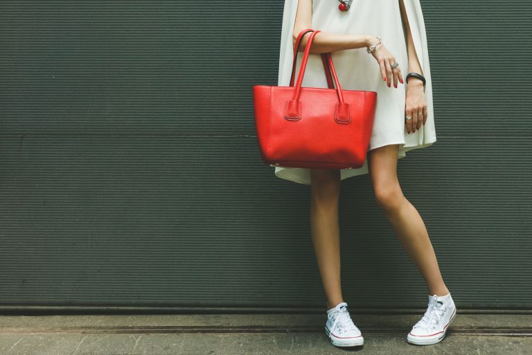 Fashionable beautiful big red handbag on the arm of the girl in a fashionable white dress and sneakers, posing near the wall on a warm summer night, What Color Shoes With a White Dress? [5 Awesome Options!]