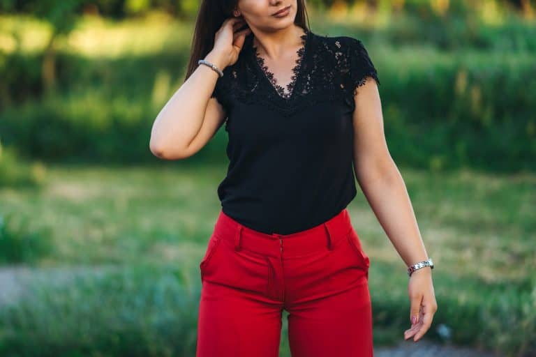 Pretty young caucasian woman posing in public park wearing red pants and black shirt, What Color Shirt Goes With Red Pants?