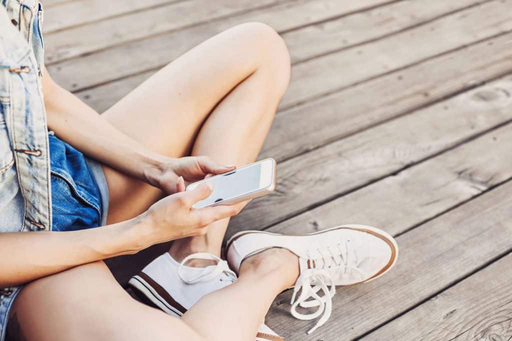 Trendy girl using smart phone, wearing white sneakers