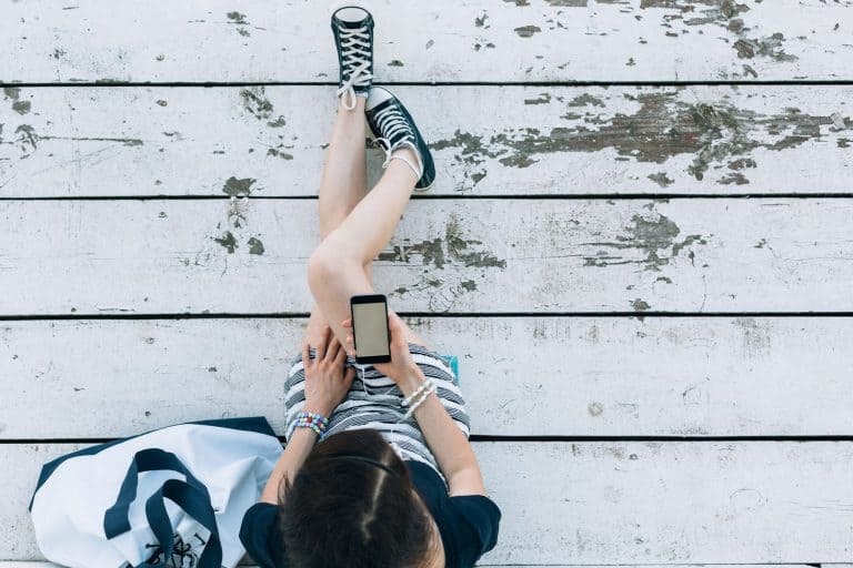 Young girl sitting at wooden planks and using smartphone, What Color Sneakers Goes With Everything?